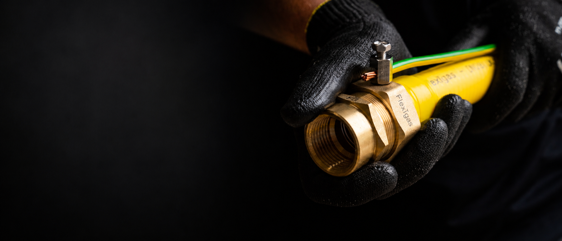 Installer's gloved hands holding the FG Bond fitting on a yellow Flexigas pipe with the earth bond cable attached